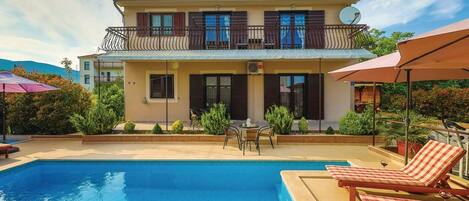 Un edificio de dos pisos con piscina, mobiliario exterior y un balcón.