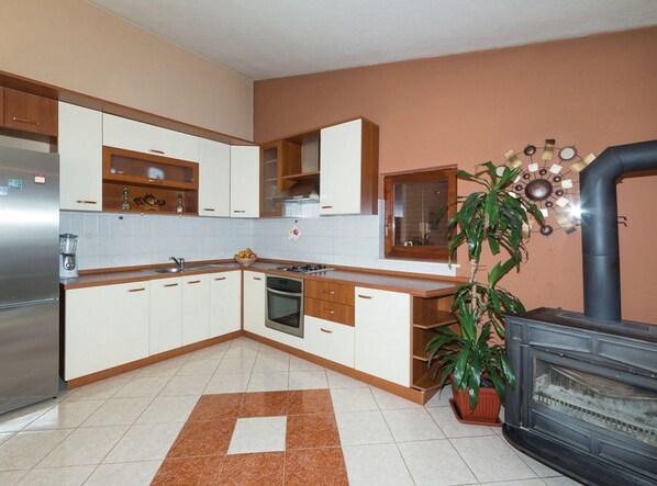 A modern kitchen with white cabinets, a stainless steel refrigerator, a stove, and a black wood-burning stove.