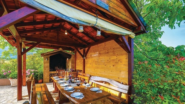 A wooden outdoor dining area with a long table set for a meal, benches, and a covered seating area. - Mediterranean Stylish Villa With Pool in Kastel Stari (Kastela)