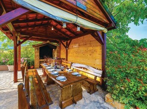A wooden outdoor dining area with a long table set for a meal, benches, and a covered seating area.