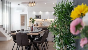Un espace de salle à manger moderne, avec une longue table, des chaises et un luminaire suspendu.