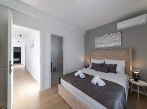 A modern hotel room with a large bed, a bedside table with a lamp, and a wall-mounted air conditioner. - Luxury Kastela Villa With Heated Pool and Lounge Area (Kastela)