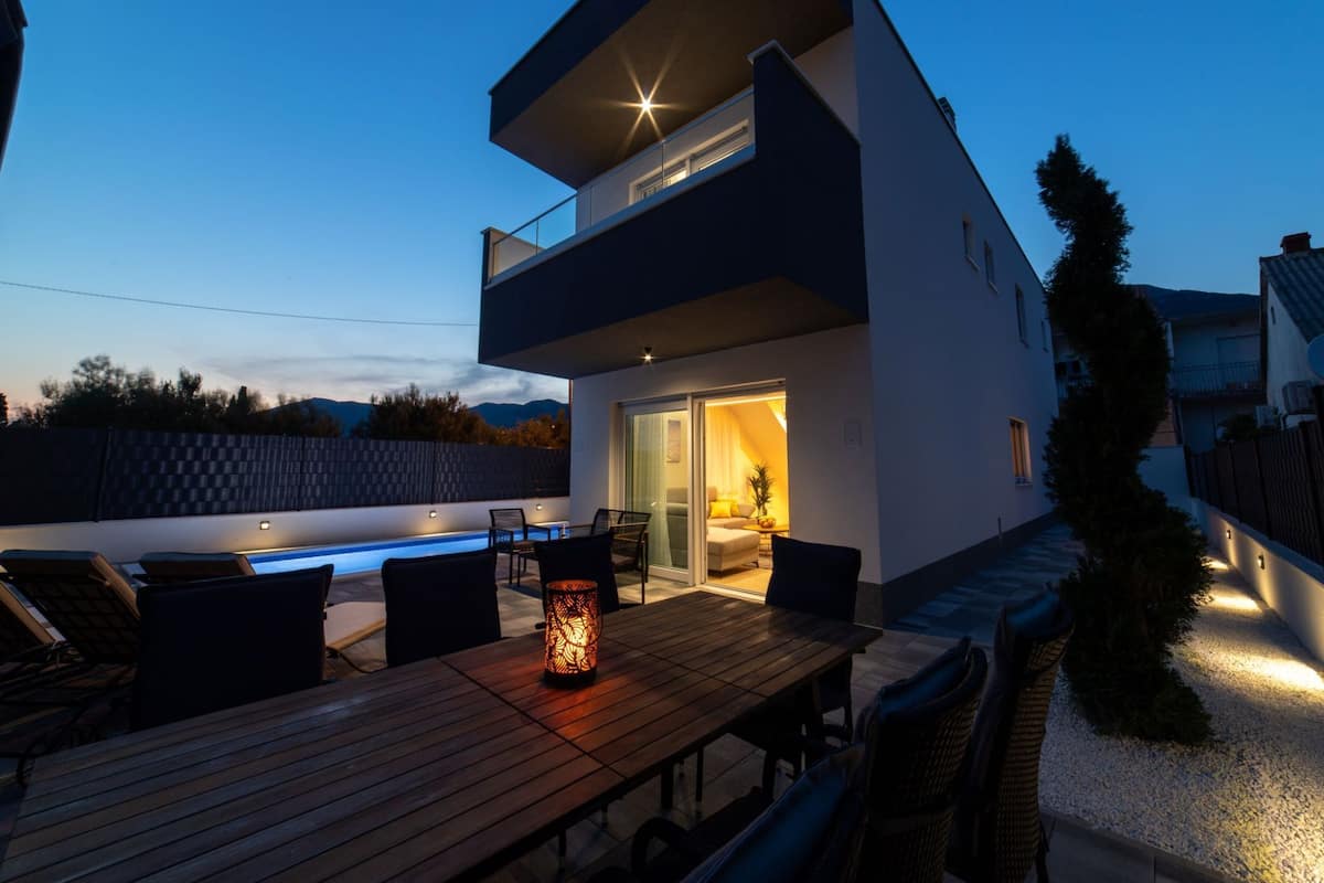 A modern two-story house with a balcony, a swimming pool, and outdoor seating.