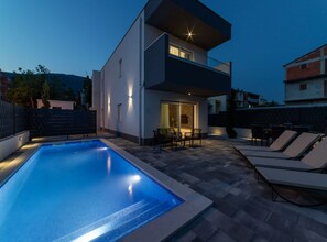 A modern two-story house with a swimming pool, outdoor seating, and a well-lit balcony. - Luxury Kastela Villa With Heated Pool and Lounge Area (Kastela)