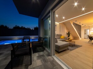 A modern living area with a pool, sliding glass doors, and a staircase leading to an upper level. - Luxury Kastela Villa With Heated Pool and Lounge Area (Kastela)