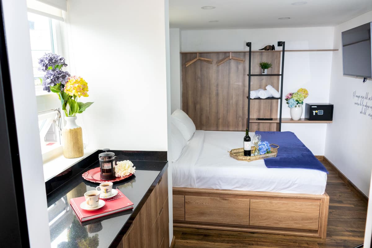 A hotel room with a bed, bedside table, and a wall-mounted shelf.