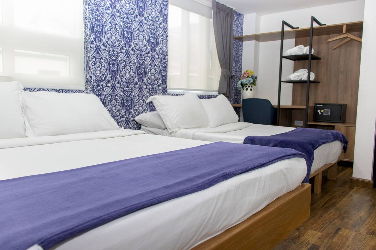 A hotel room with two single beds, a wooden wardrobe, a desk, and a chair.