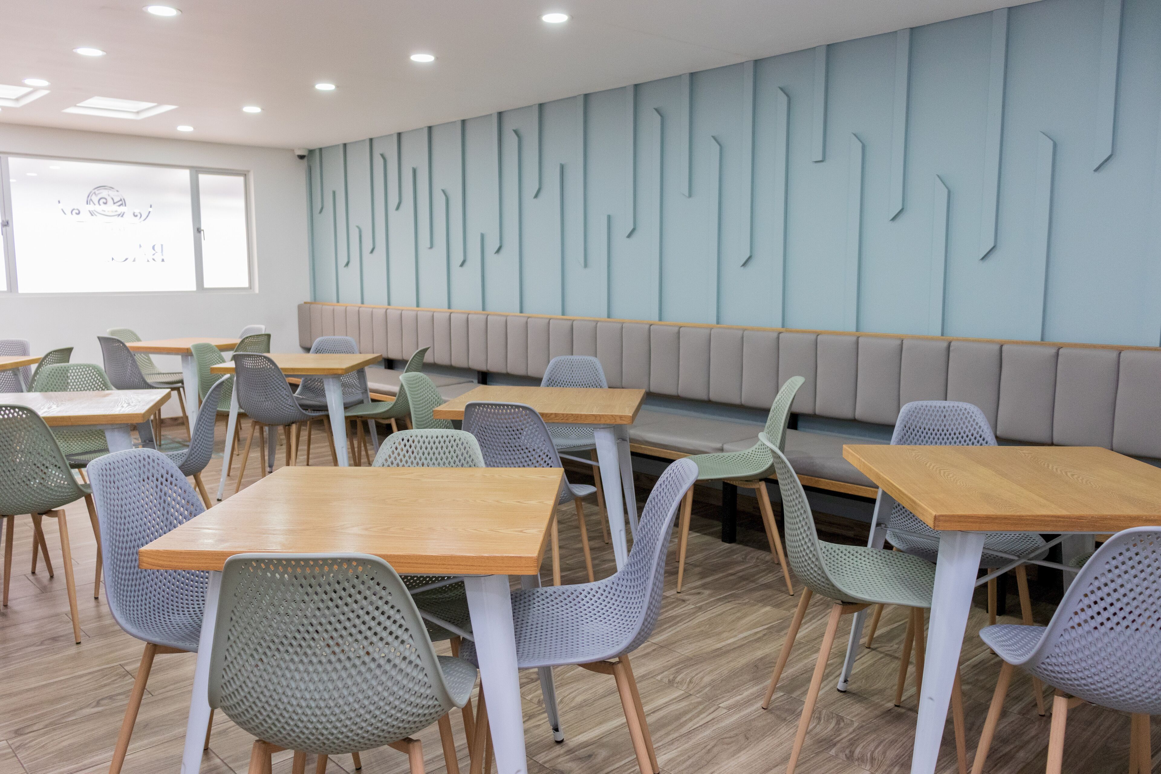 Ein moderner Essbereich mit Holztischen und grünen Stühlen, eine Sitzbank an der Wand und einem Wanddesign mit Muster.