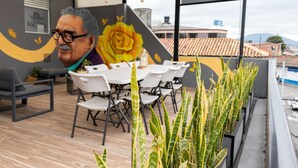 Eine Terrasse mit Tisch und Stühlen, ein Wandgemälde mit einer großen gelben Rose und ein Blick auf eine Stadtlandschaft mit einem Hotel im Hintergrund.