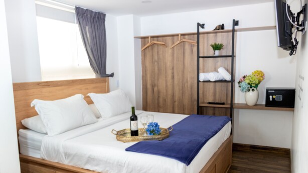 Ein ordentlich bezogenes Bett mit einem Weintablett, einer blauen Decke und einer Blumenvase.