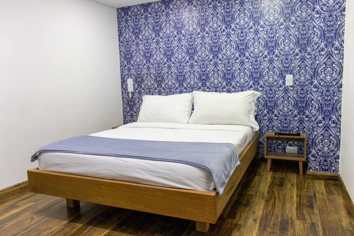 A bedroom with a wooden bed, white bedding, and a blue patterned wallpaper.