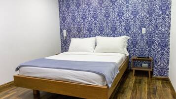 Une chambre à coucher avec un lit en bois, du linge de lit blanc et un papier peint à motifs bleus.