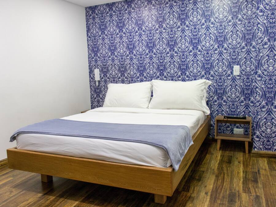 Une chambre à coucher avec un lit en bois, du linge de lit blanc et un papier peint à motifs bleus.