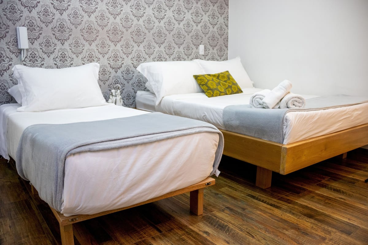 Two single beds with wooden frames, white bedding, and a patterned wallpaper background.