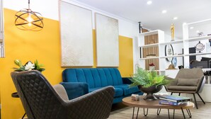 Ein modernes Wohnzimmer mit einem blauen Sofa, einem dunklen Sessel, einem Couchtisch mit Büchern und einer Zimmerpflanze.