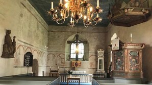 Interior de igreja com bancos, lustre, estátua e relógio.