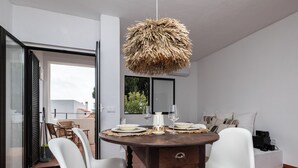 A dining area with a round wooden table, white chairs, and a unique thatched ceiling light.