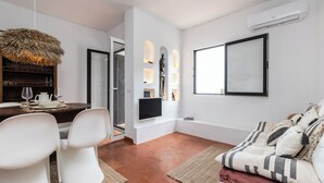 A modern living room with a dining area, a TV mounted on the wall, and a large window.