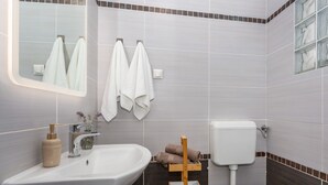 A bathroom with a sink, mirror, towel rack, toilet, and a small wooden shelf. - Apartment Anivija (Omisalj)