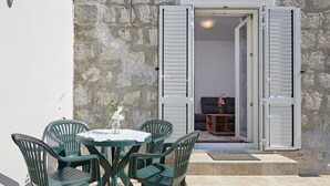 A patio with a round table and chairs, a vase with flowers, and a stone wall. - Cozy Downtown Trogir Apartment With Balcony (Trogir)