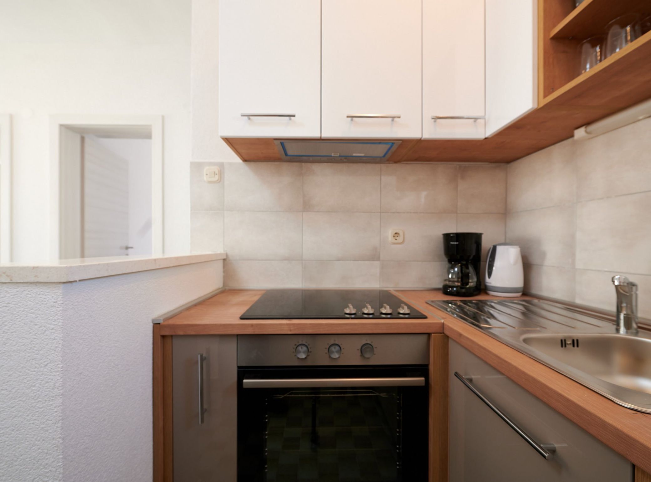 A compact kitchen with a built-in oven, a stovetop, a coffee maker, and a sink.