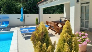Area piscina con lettini, un tavolo in legno e piante in vaso.