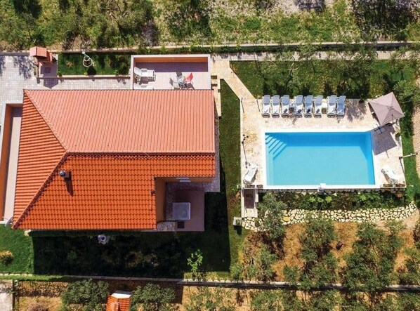 An aerial view of a house with a red-tiled roof, a swimming pool, and a patio with lounge chairs.