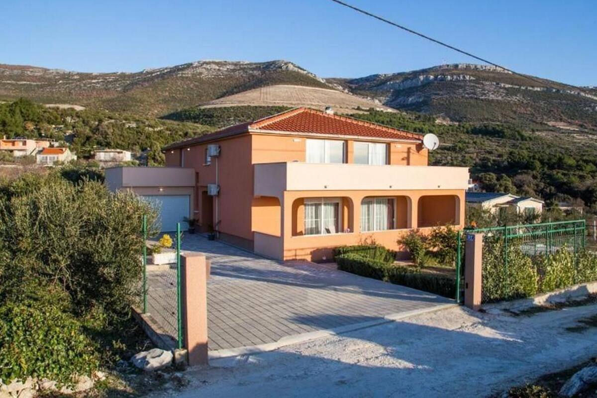 A two-story house with a tiled roof, a satellite dish, and a paved driveway.