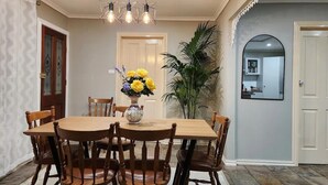 Uma sala de jantar com uma mesa de madeira redonda, seis cadeiras de madeira, um vaso com flores amarelas e uma luminária pendente moderna.