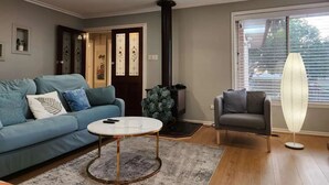Uma sala de estar com sofá, mesa de centro, poltrona, ventilador e janela com persianas.