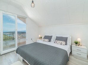 Relax in this serene bedroom with a large bed, nightstand, and potted plant, offering a peaceful view from the sliding glass door to the outdoor balcony.