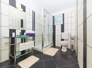 Bathroom features a glass shower enclosure, white toilet, and glass sink.