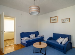 A living room with two blue sofas, a small wooden coffee table, and a ceiling light fixture. - Modern Apartment Near Trogir Beach With Sea View Terrace and Lounge Area (Trogir)