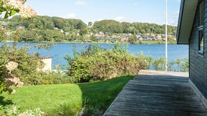 Uma propriedade à beira do lago com deck de madeira, vegetação exuberante e vista para o lago e casas ao longe.