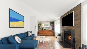 Un salon moderne avec un canapé bleu, une cheminée et un grand téléviseur fixé au mur.