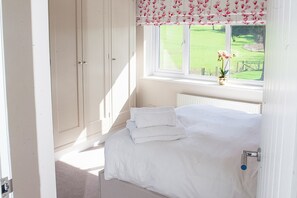 A bedroom with a bed, a window with a view of a green field, and a radiator.
