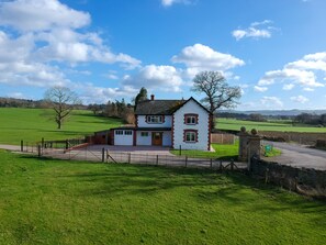 A white house with a red door and windows, surrounded by a green field and a stone wall.