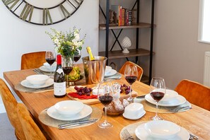A dining table set with plates, glasses, a bottle of wine, a vase with flowers, and a fruit bowl.