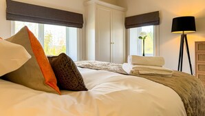 Quarto de hotel com cama, travesseiros, mesa de cabeceira, abajur e janela com vista para árvores.