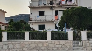 A multi-story residential building with balconies, a stone wall in the foreground, and a mountainous backdrop. - Spacious Apartment Steps From the Beach, With Private Terrace and Grill (Kastela)