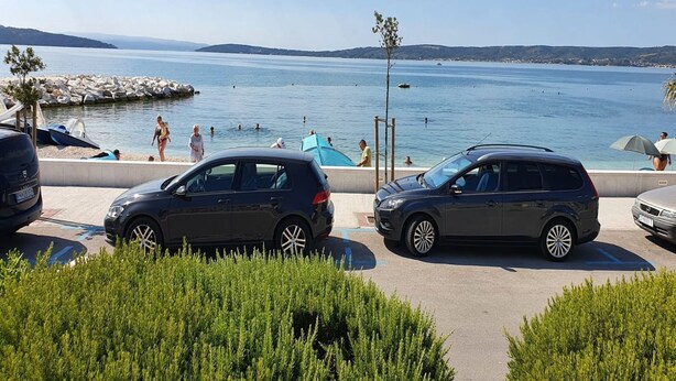 A parking area with cars, a beach, and a clear sky. - Spacious Apartment Steps From the Beach, With Private Terrace and Grill (Kastela)