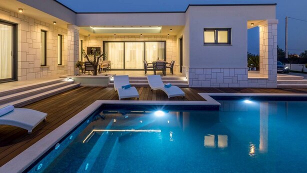Ein modernes Haus mit Schwimmbad, Liegestühlen und einer Terrassenanlage.