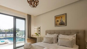 Ein Hotelzimmer mit einem großen Bett, einem Schminktisch mit Beleuchtung, einem Gemälde und Blick auf einen Swimmingpool.