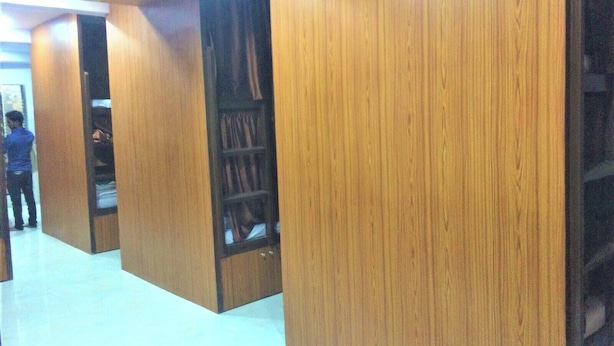 A library with wooden bookshelves and a person standing in the background. - Neon Nest Dormitory Suits (Mumbai)