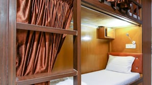 A compact, well-lit room with a single bed, a small cabinet, and a wall-mounted lamp. - Neon Nest Dormitory Suits (Mumbai)