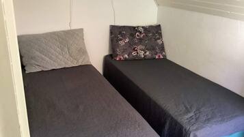 Ein kleines Zimmer mit einem Einzelbett, einem gesteppten Kissen und einem blumigen Kissen.