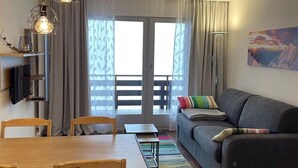 Ein modernes Wohnzimmer mit einer Couch, einem Esstisch mit Stühlen und einem großen Fenster mit Vorhängen.