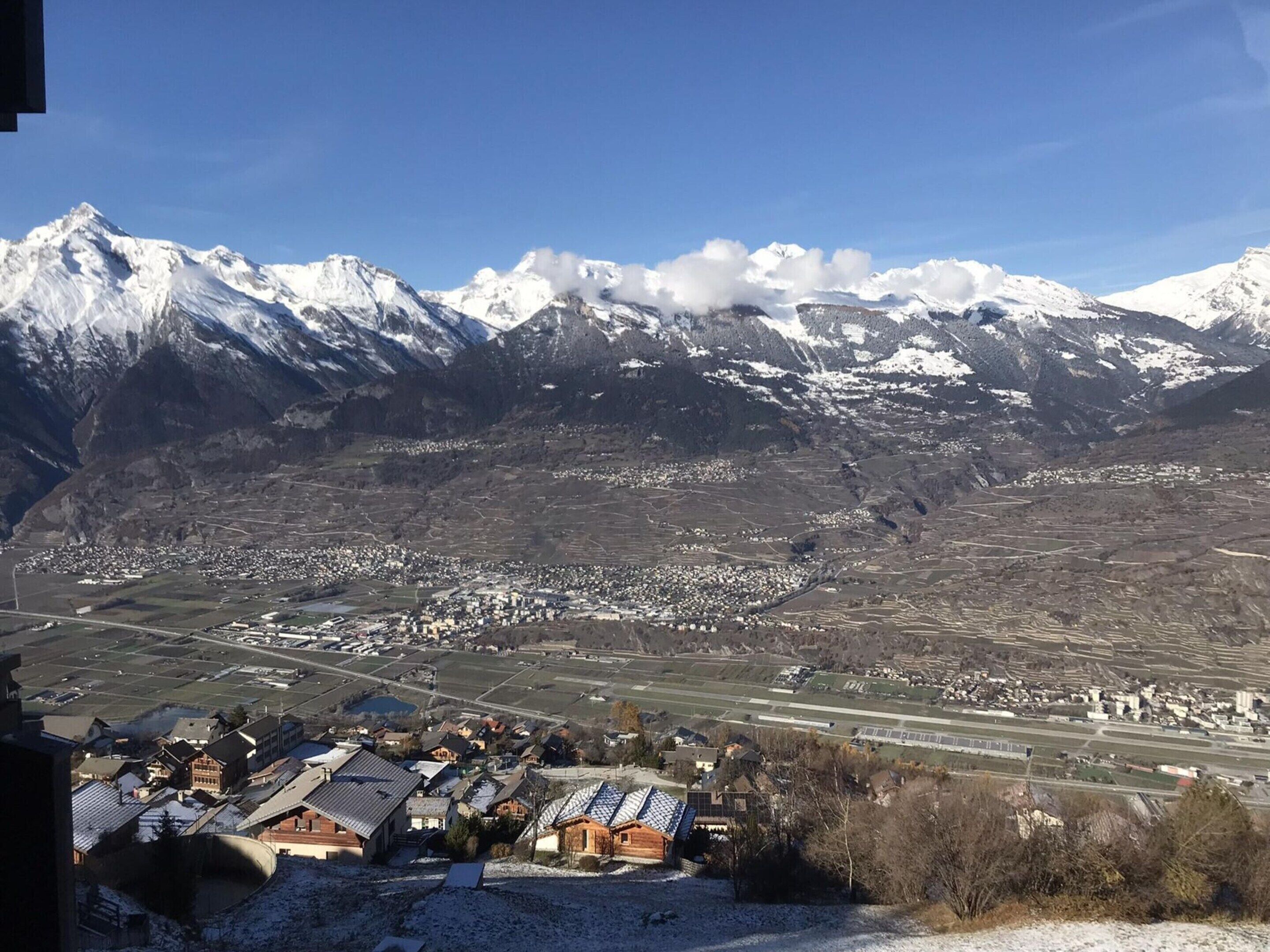 A mountainous landscape with snow-covered peaks and a valley with scattered buildings.