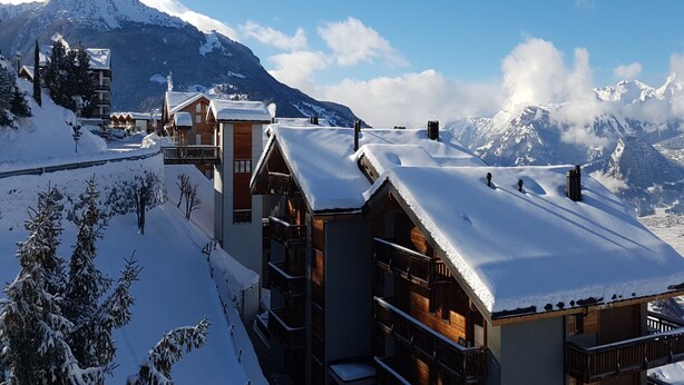 Ein schneebedecktes Bergresort mit Holzbauten, darunter eine Chalet und eine Lodge, mit freiem Blick auf die umliegenden Berge.