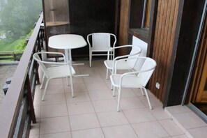 A balcony with a white table and four white chairs, a wooden door, and a view of greenery. - Charming Apartment With Hill View (Veysonnaz)